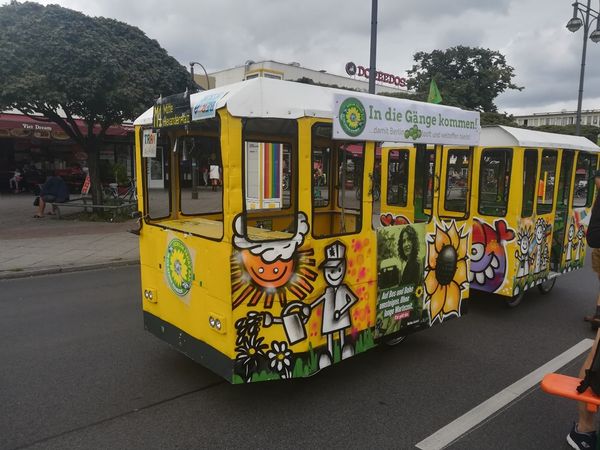 Two wagons coupled together are standing on the road at Kurt-Schumacher-Platz. The appearance is reminiscent of the yellow Tatra trams in Berlin. There is a sign on the front: M4 Mitte Alexanderplatz. There are colorful graffiti on the side oft he wagons